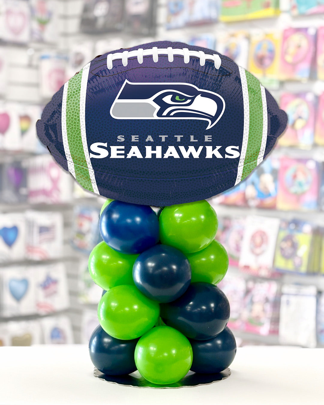 Tabletop balloon centerpiece of a Seattle Seahawks football mylar stitting on a small column of 5" lime green and navy blue latex balloons.